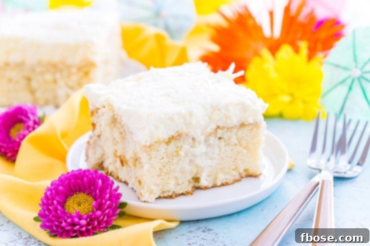 Close-up of a slice of Coconut Poke Cake on a plate, showing the moist cake layers and creamy white frosting.