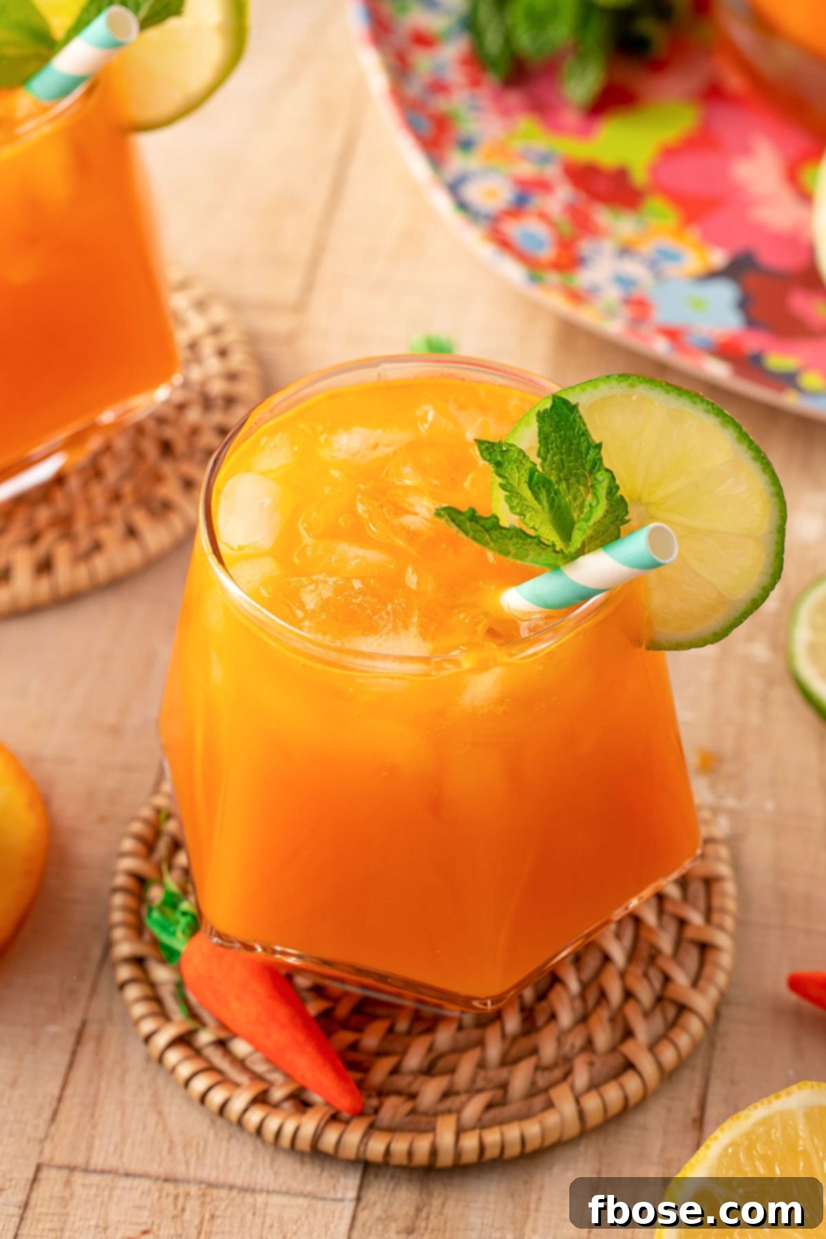 A close-up view of a glass of sparkling orange Easter punch, garnished with a vibrant citrus slice, resting on a textured rattan coaster.