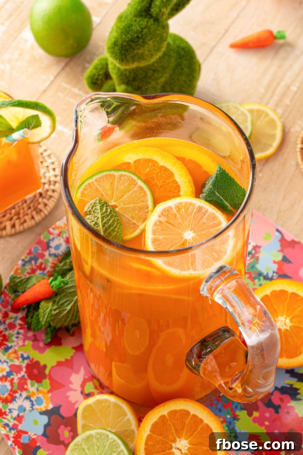 Close up of a large pitcher overflowing with bright orange and carrot punch, beautifully garnished with an assortment of fresh citrus slices on a rustic wooden table, ready for serving.