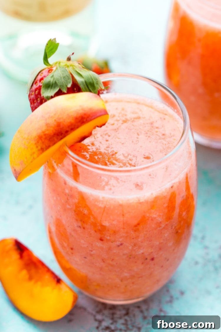 A vibrant Strawberry Peach Wine Slushie in a glass, garnished with fresh fruit, perfect for summer gatherings.