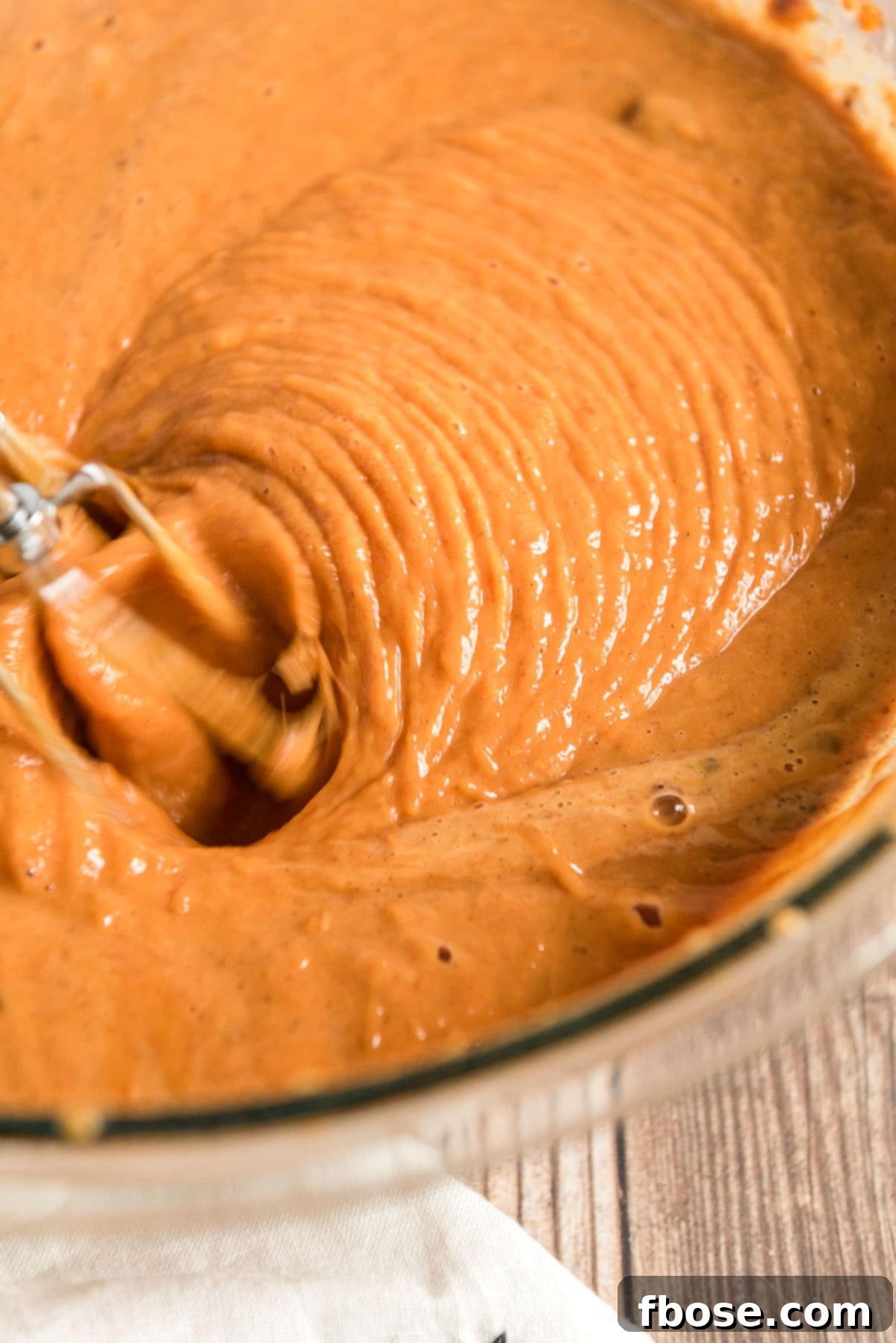 Pumpkin cake batter being mixed with a hand mixer in a large mixing bowl.