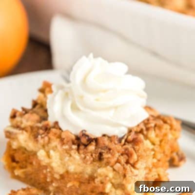 Close up photo of a slice of pumpkin dump cake on a white plate with pumpkin and more cake in background.