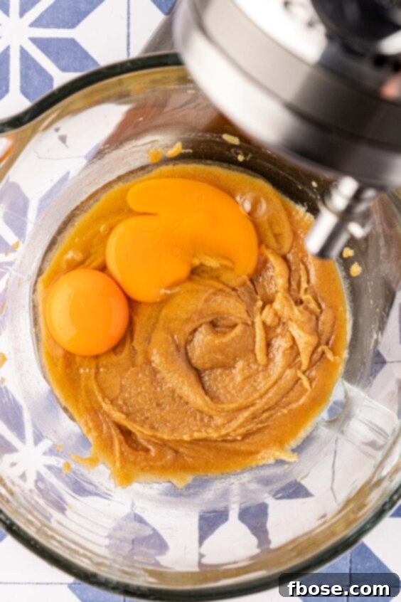 Eggs being added to wet ingredients in a mixing bowl for chocolate chip cookies.