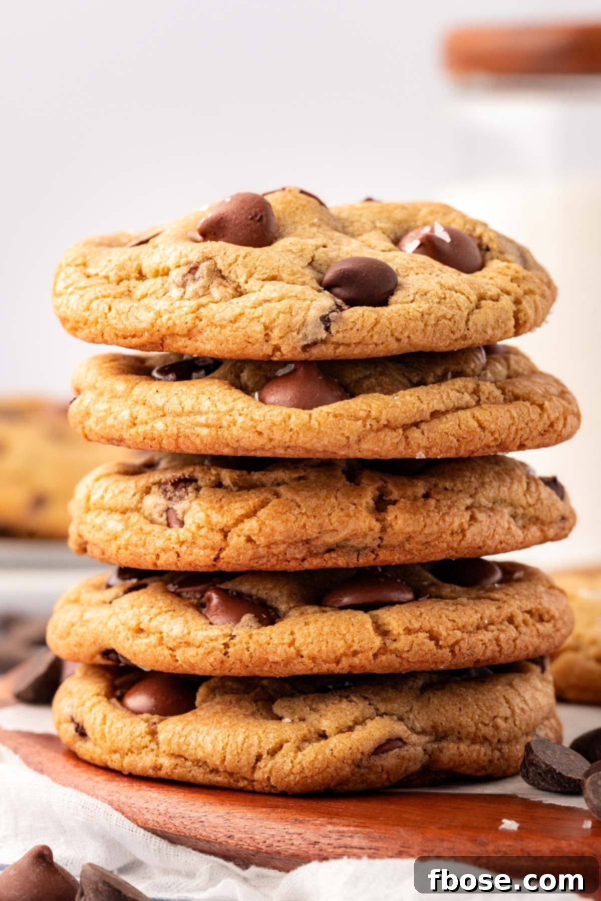 A stack of 5 thick and chewy bakery-style chocolate chip cookies on a table, perfectly golden brown.