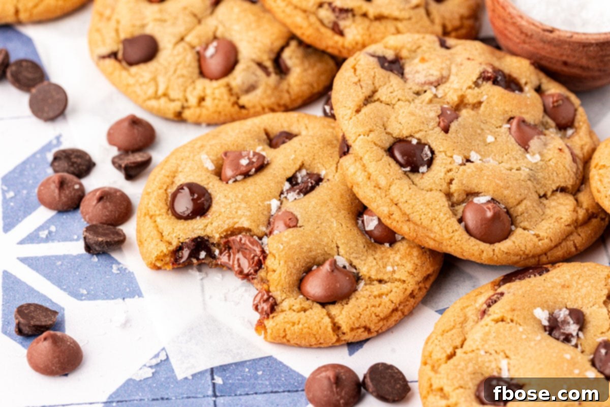 Close up of a plate of thick and chewy chocolate chip cookies with a sprinkle of flaky sea salt, showing their rich texture.