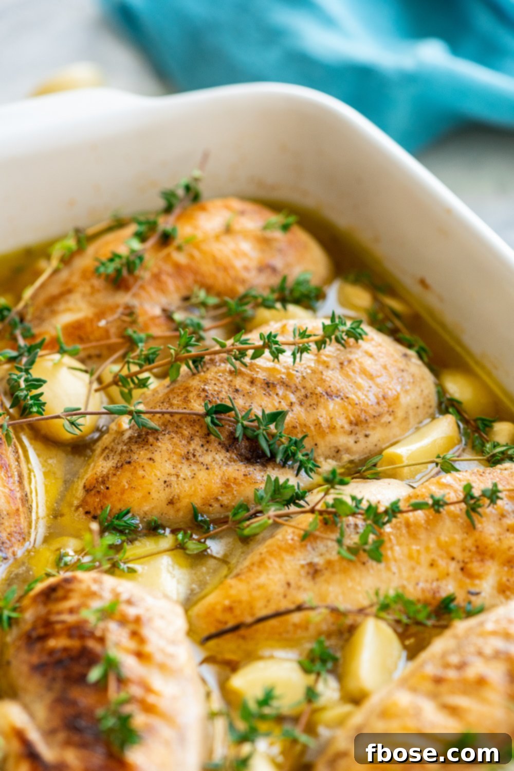Roasted Garlic Chicken in a white casserole dish with blue napkin