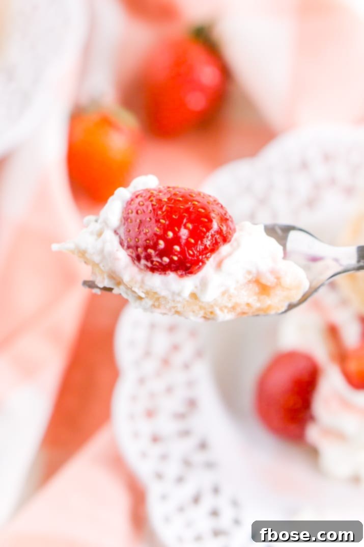 Close up photo of a fork with a perfect bite of strawberry shortcake on it, highlighting the layers of biscuit, cream, and strawberries.