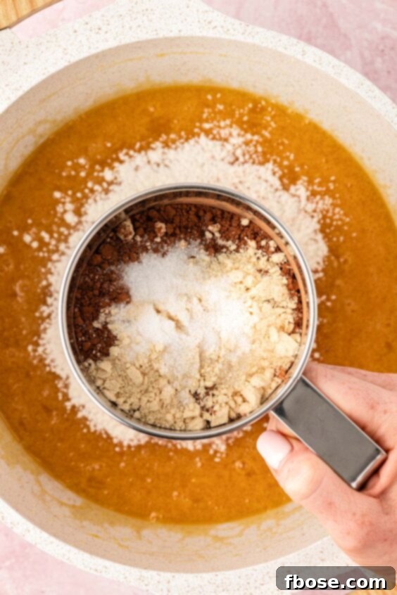Dry ingredients being sifted into wet ingredients for brownies.