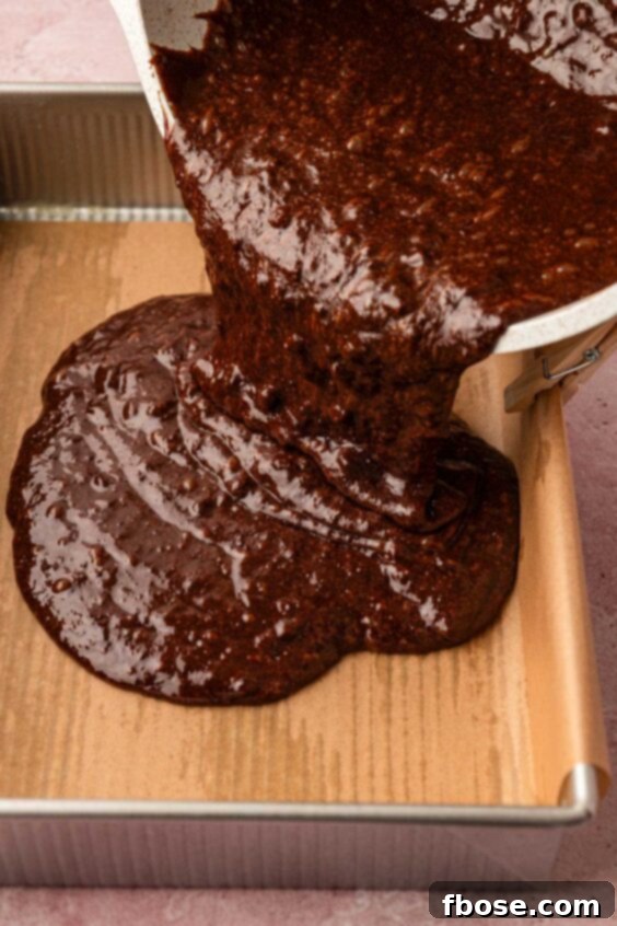 Brownie batter being poured into a prepared baking pan.