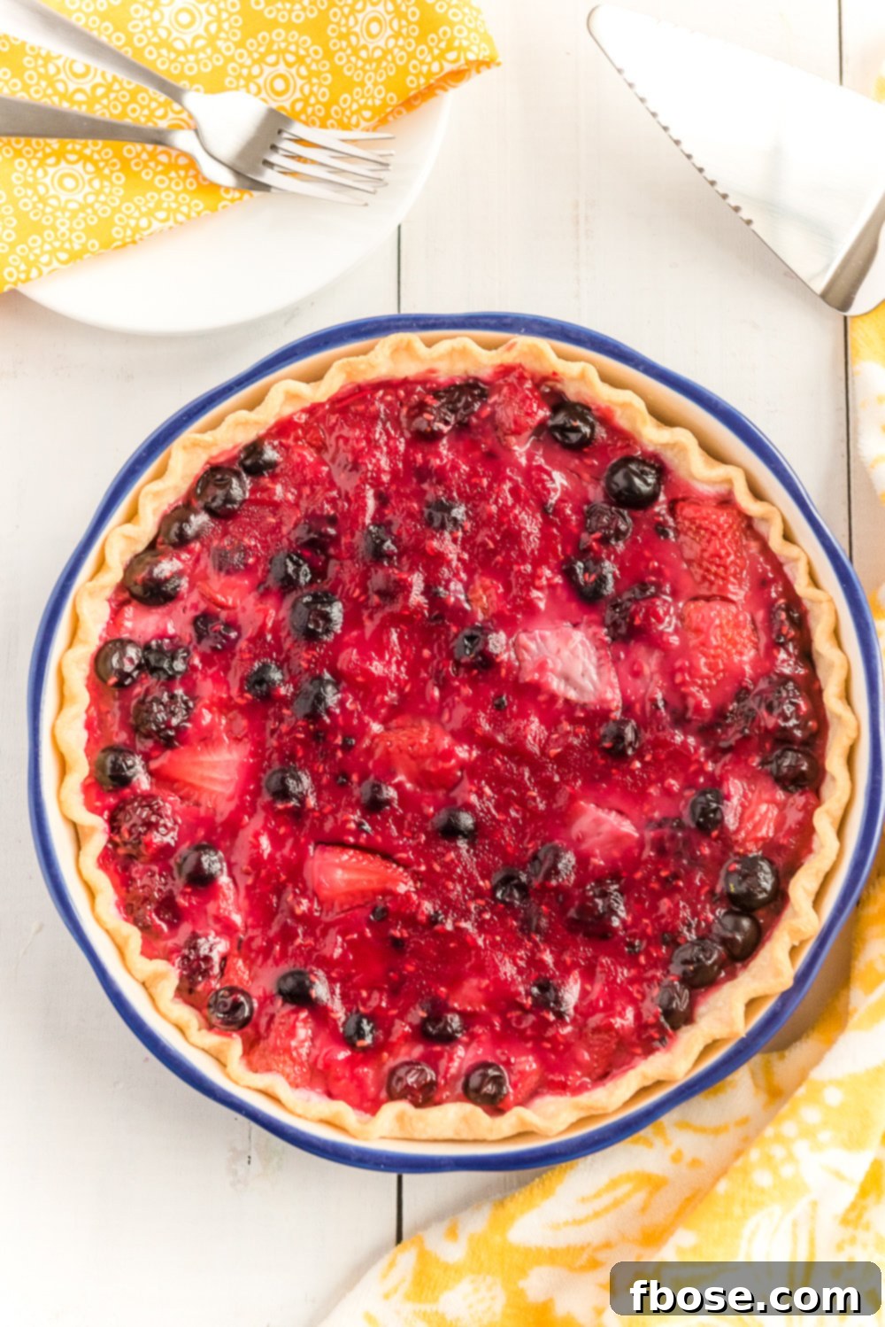 Overhead shot of a whole Mixed Berry Pie on white wood table.