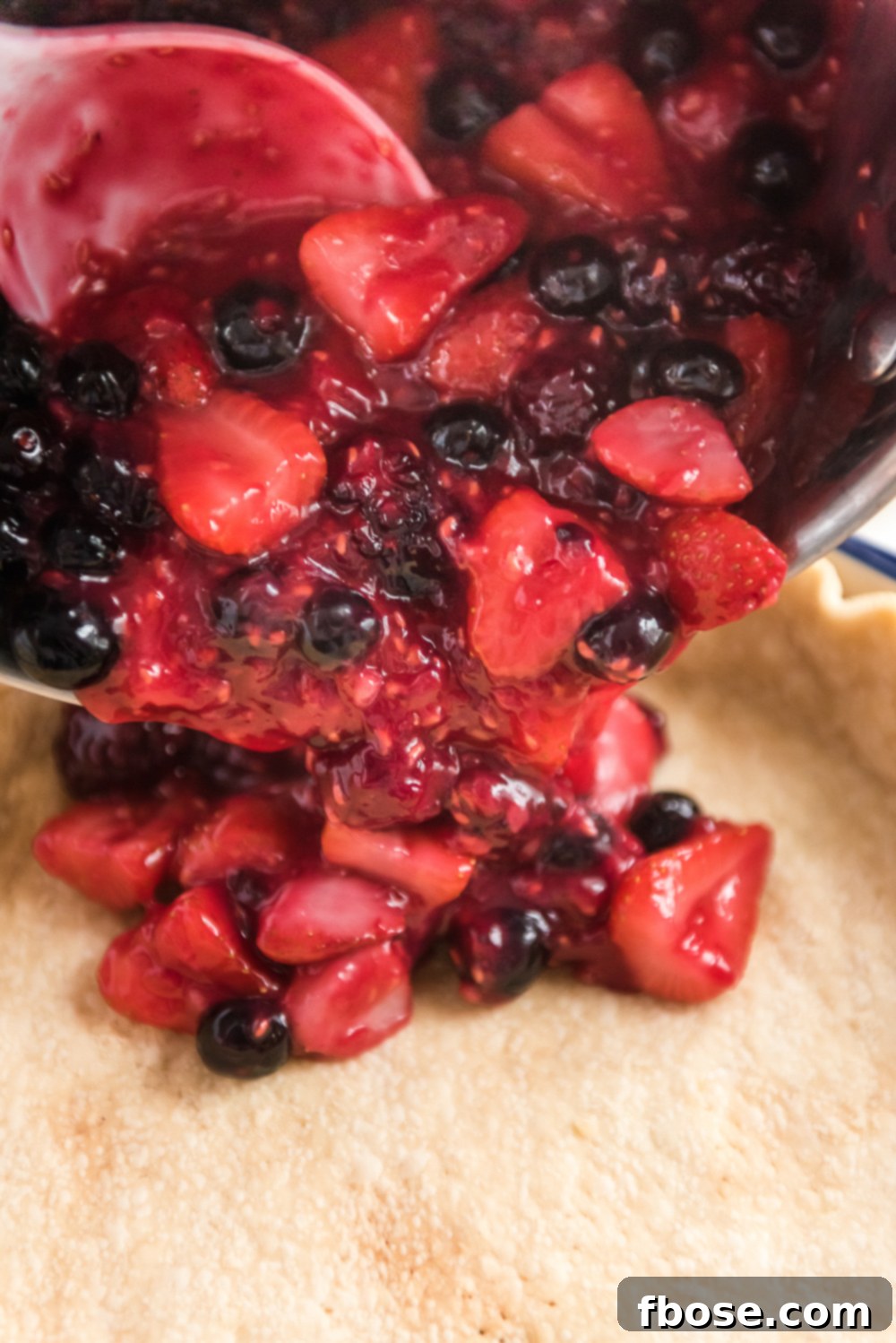 Mixed Berry Pie filling being poured into a prepared pie crust.