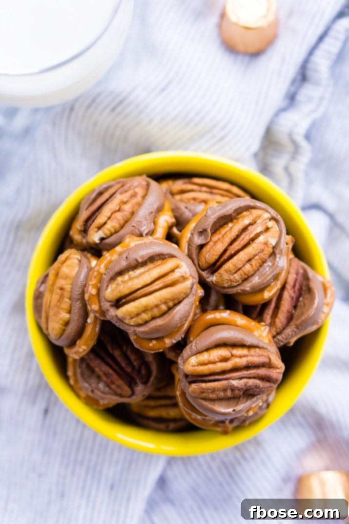 A baking sheet filled with rows of mini pretzels, each topped with a Rolo candy, ready to be baked into delicious Pretzel Turtles.
