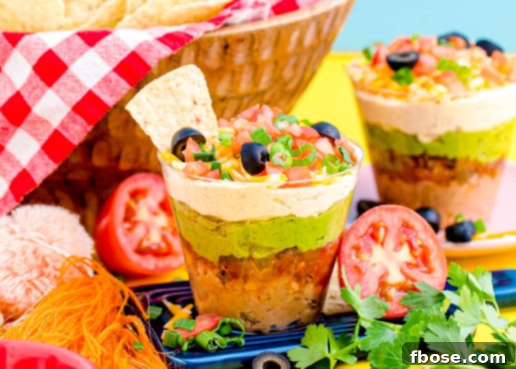 Close-up of a 7 Layer Dip Cup with a tortilla chip scooping into it, highlighting the distinct layers.