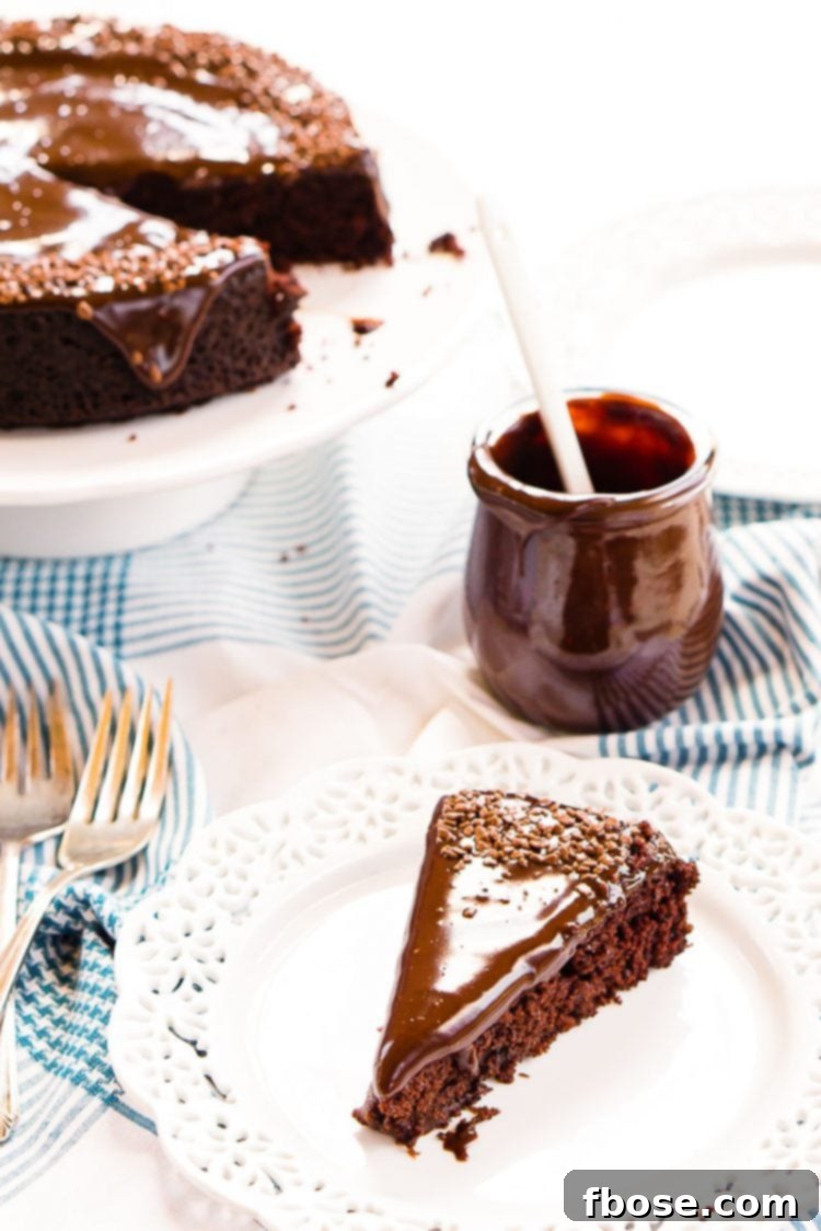 Slice of chocolate depression cake on a white plate with a jar of icing and the rest of the cake on a cake stand behind it.