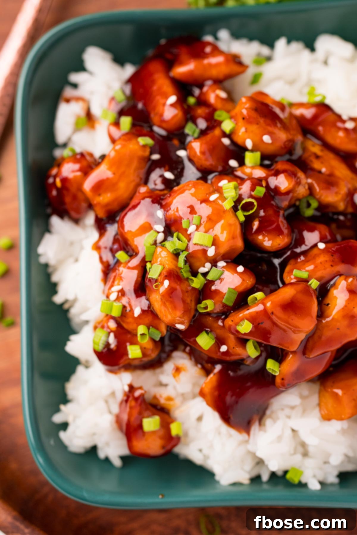 Effortless Bourbon Chicken 2 Close up photo of bourbon chicken on a bed of rice on a teal green dish.