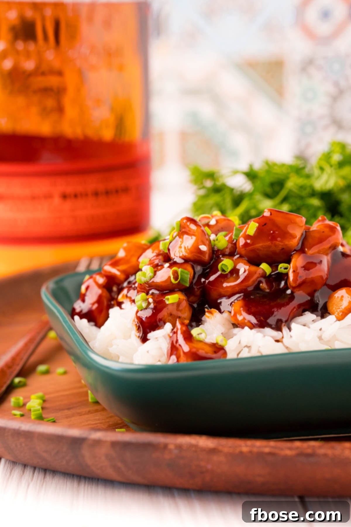 Effortless Bourbon Chicken 6 Close up photo of bourbon chicken and rice on a green plate on a wooden platter.