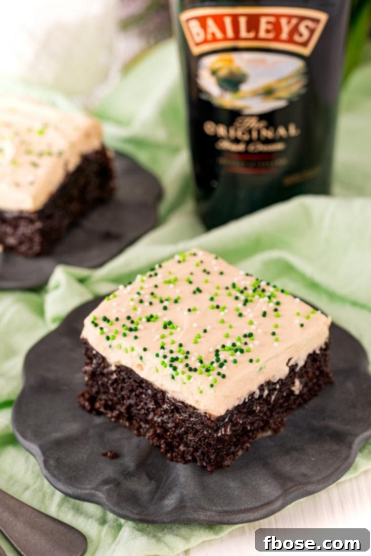 A slice of Irish cream cake on a black plate with a bottle of Bailey's in the background, emphasizing its adult nature.