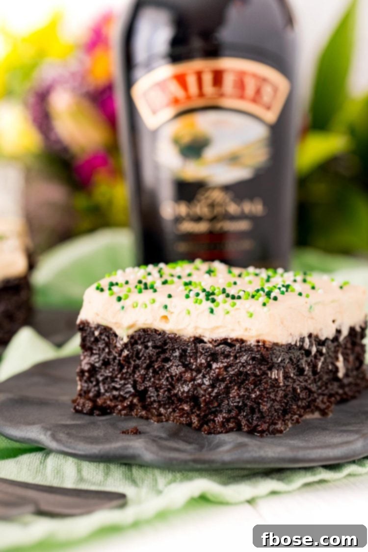 Close up photo of Irish Cream Cake on a black plate with a bottle of Bailey's in the background, highlighting the creamy texture.
