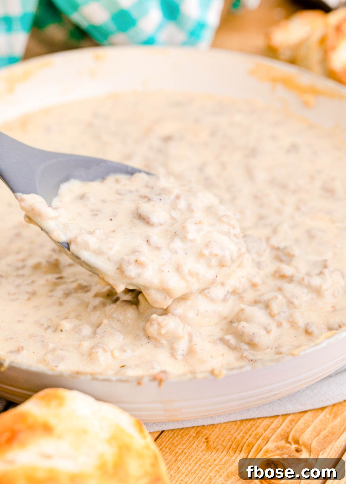 Close up shot of creamy, rich sausage gravy being generously spooned from a cast iron skillet into a serving bowl.