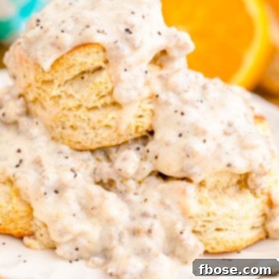 Close up photo of fluffy homemade buttermilk biscuits generously covered with rich, creamy sausage gravy on a white plate, ready to be served.