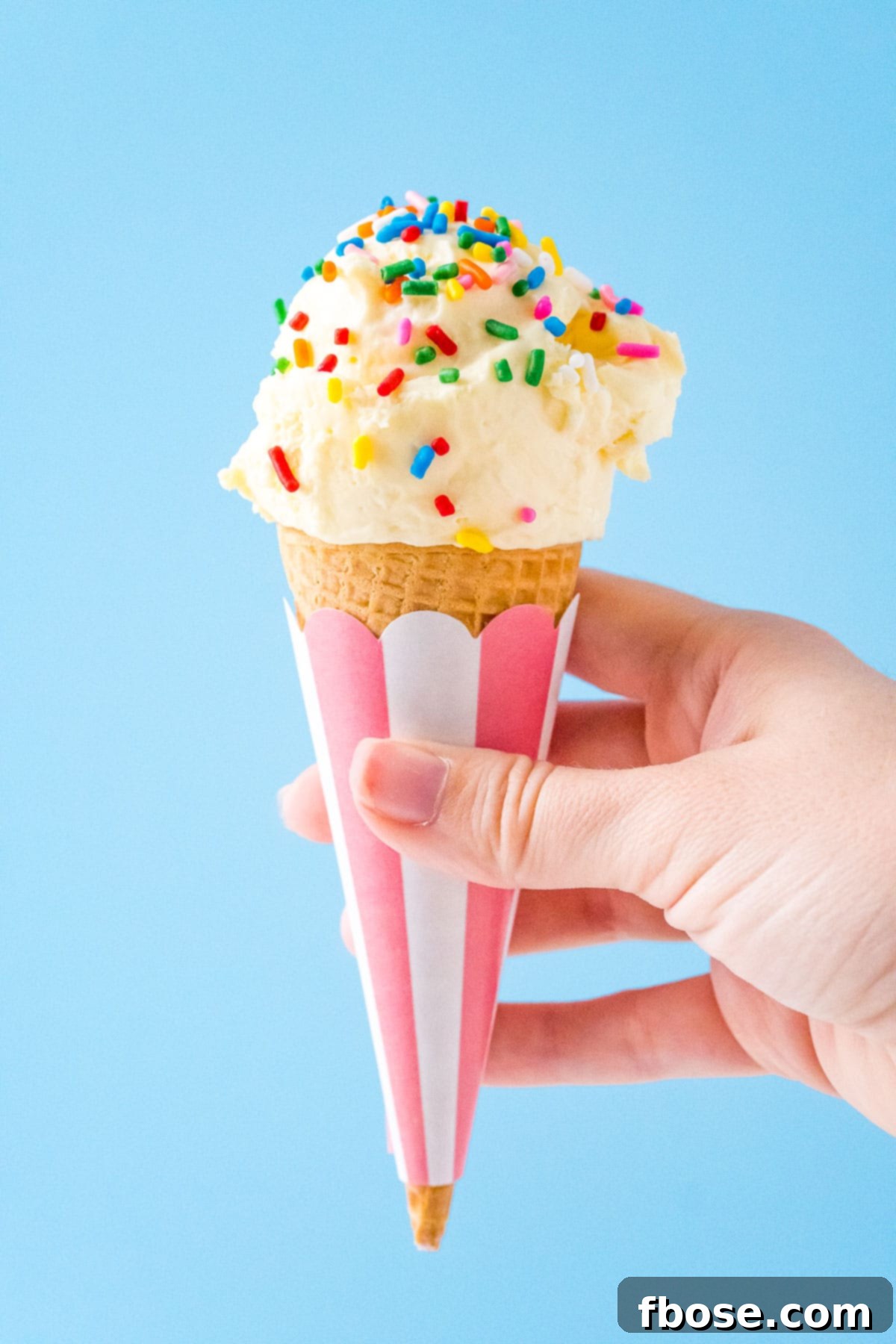 Woman's hand holding a cone of vanilla ice cream with sprinkles on it.