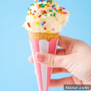 Woman's hand holding a cone of vanilla ice cream with sprinkles on it.