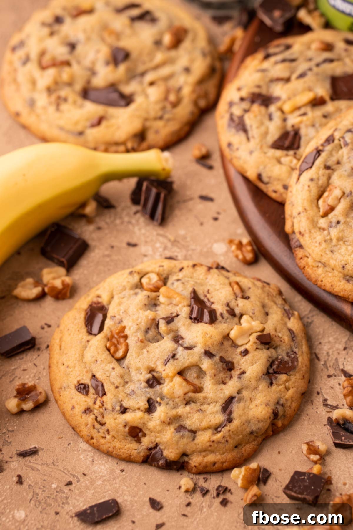 Decadent Chunky Monkey Pudding Cookies 11 Chunky Monkey Cookies on a table with chocolate, walnuts, and banana around it.