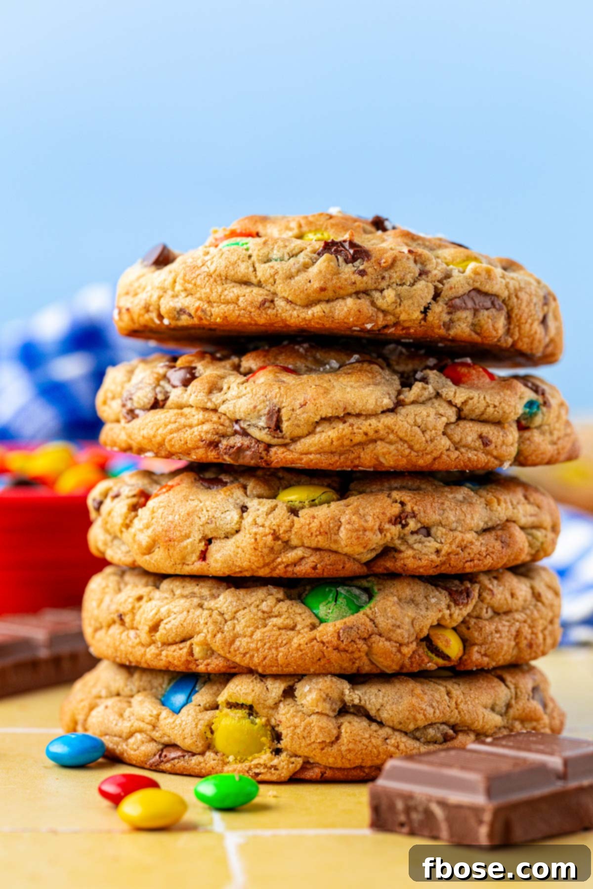 A stack of 5 large monster cookies on a yellow surface.