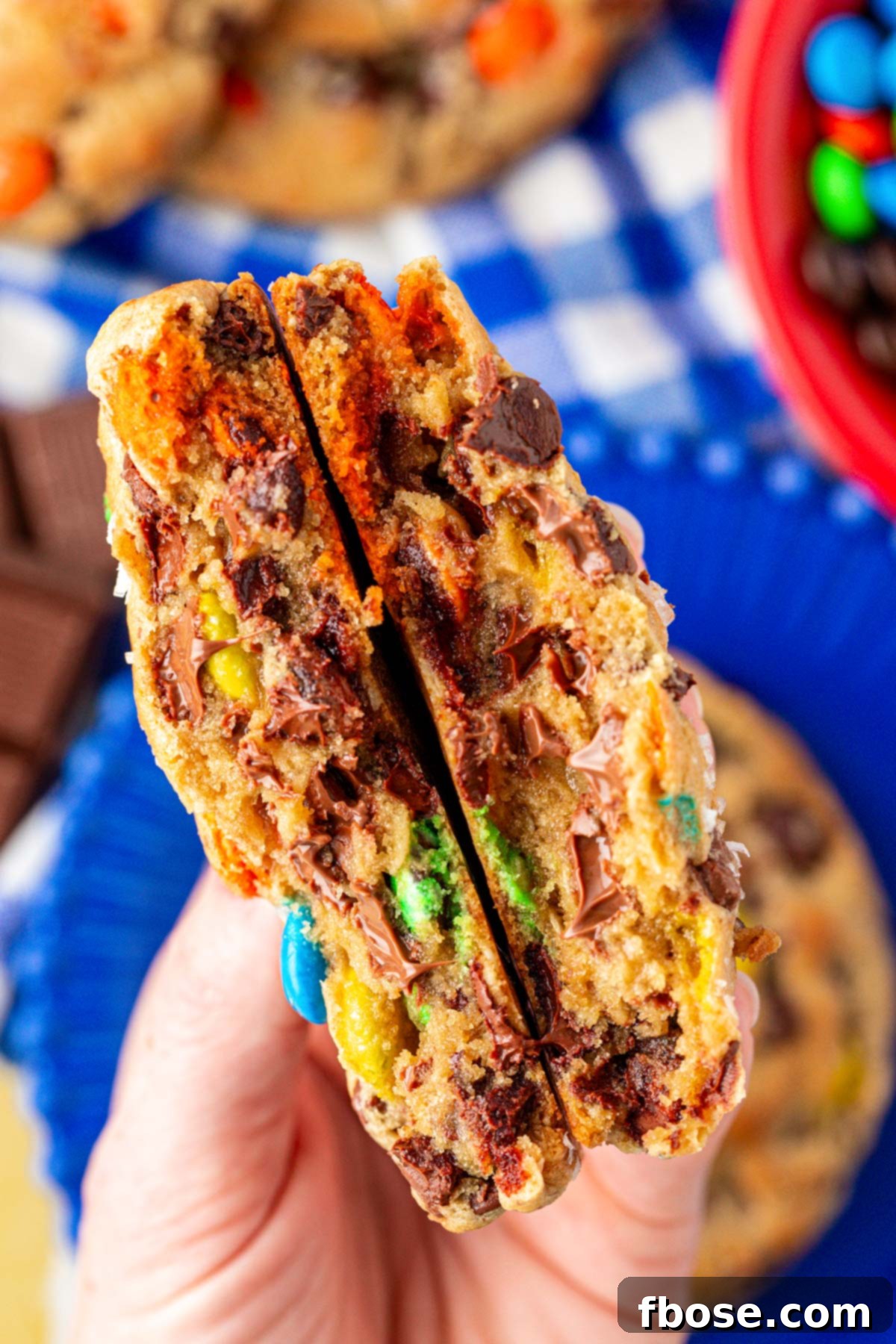 A woman's hand holding a large monster cookie that has been broken in half to the camera.