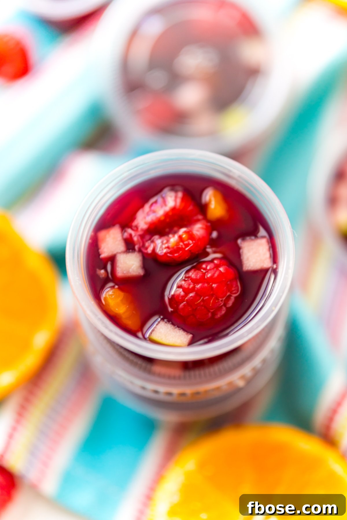 Sangria Jello Shots stacked on top of each other on a blue napkin with fruit scattered around.