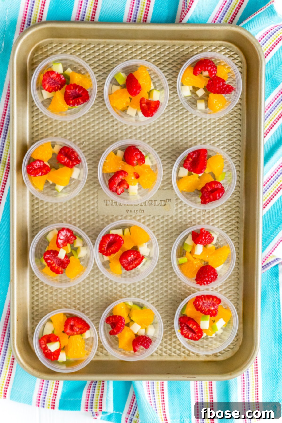 Jello shot cups filled with fruit on a baking sheet.