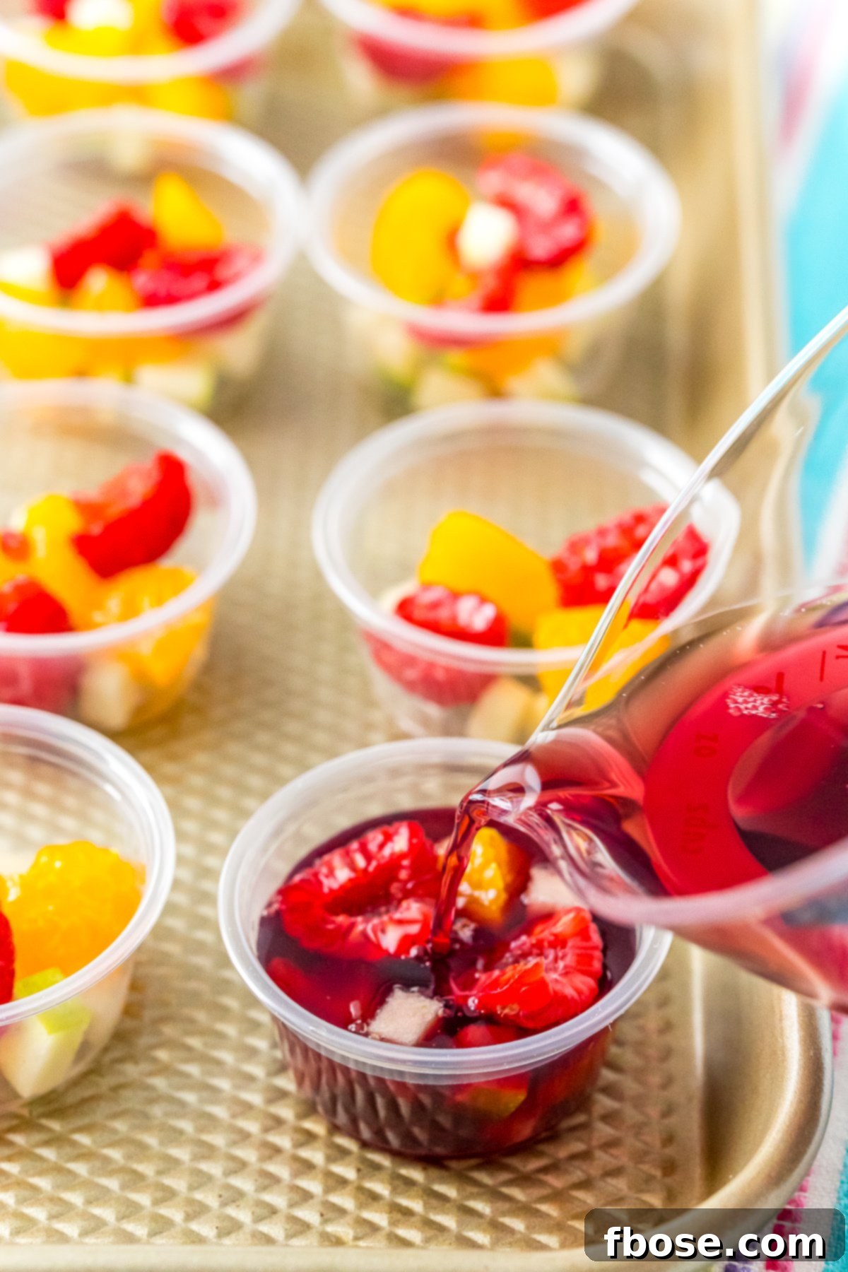 Wine jello mixture being poured into a jello shot cup filled with fruit.