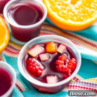 Sangria jello shots on a blue striped napkin with more jello shots and fruit scattered around.
