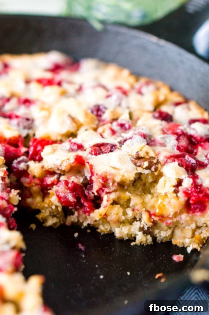 A slice of Cranberry Skillet Cake being served on a white plate, highlighting the vibrant cranberries and walnuts within the tender crumb.