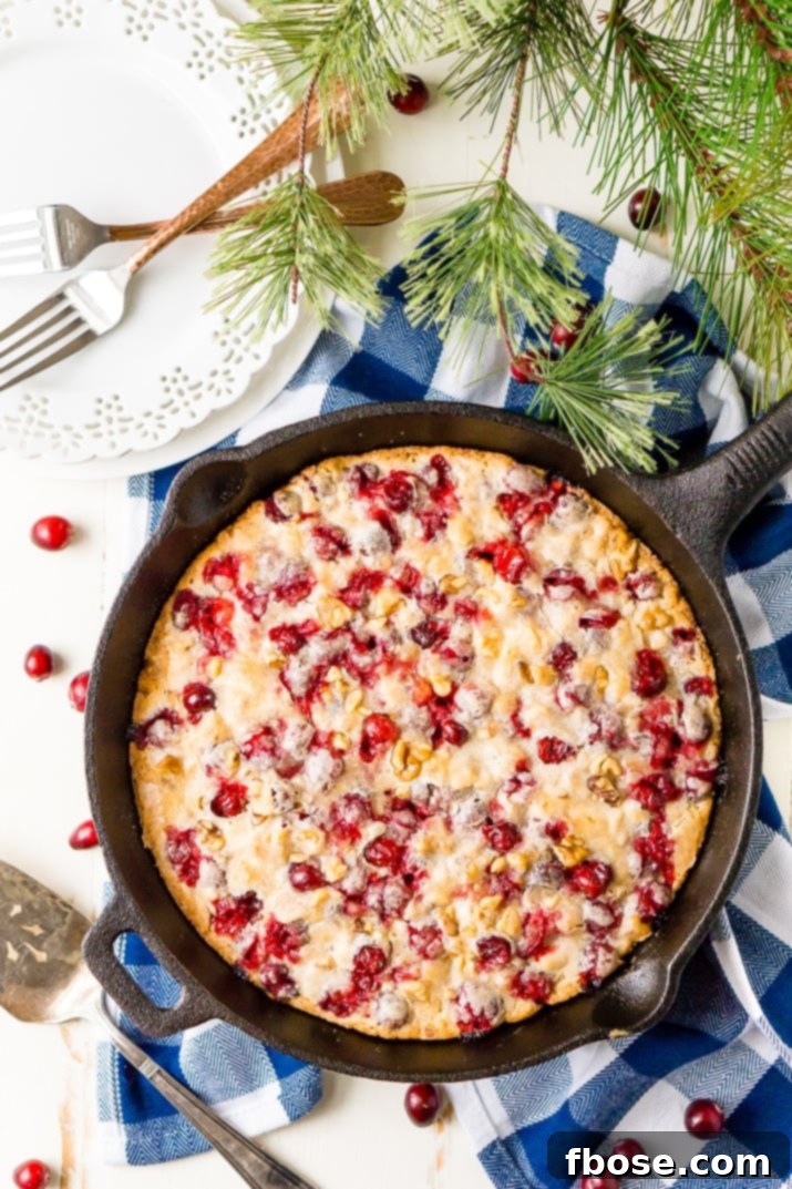 An overhead shot of the baked Cranberry Skillet Cake, showcasing its perfectly golden-brown surface, generously topped with cranberries and walnuts.