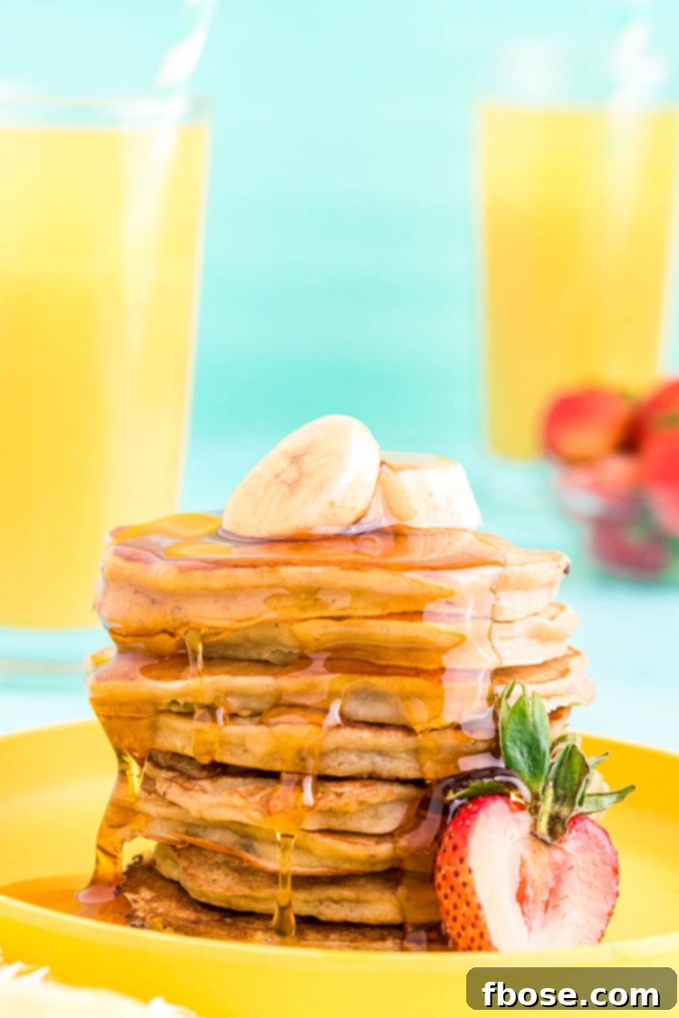 A stack of golden brown banana pancakes on a yellow plate, garnished with fresh banana slices and a strawberry, drizzled with maple syrup.