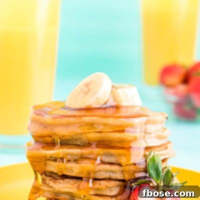 A stack of golden brown banana pancakes on a yellow plate, garnished with fresh banana slices and a strawberry, drizzled with maple syrup.