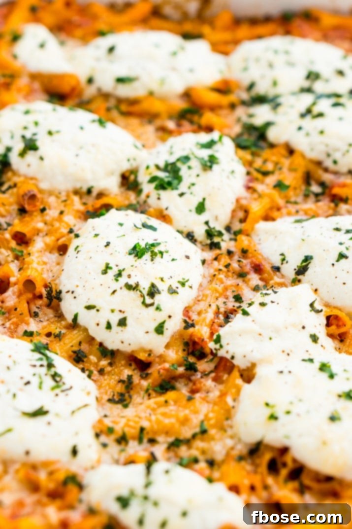 Close-up shot of baked penne pasta with creamy ricotta cheese, rich tomato sauce, and fresh basil garnish, highlighting the texture.