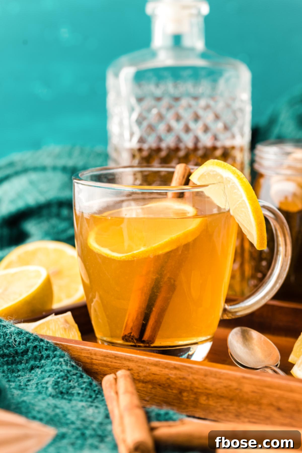 A hot toddy garnished with a lemon slice and a cinnamon stick in a clear glass mug on a rustic wooden tray.