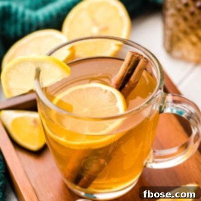 A hot toddy in a clear glass mug with lemon slice and cinnamon stick.