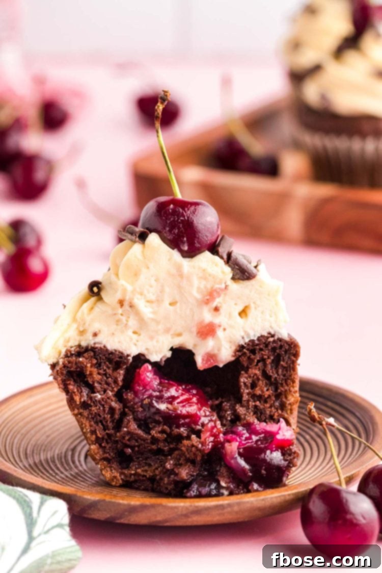 A delectable Black Forest Cupcake, cut in half to reveal its rich cherry filling, resting elegantly on a rustic wood plate.