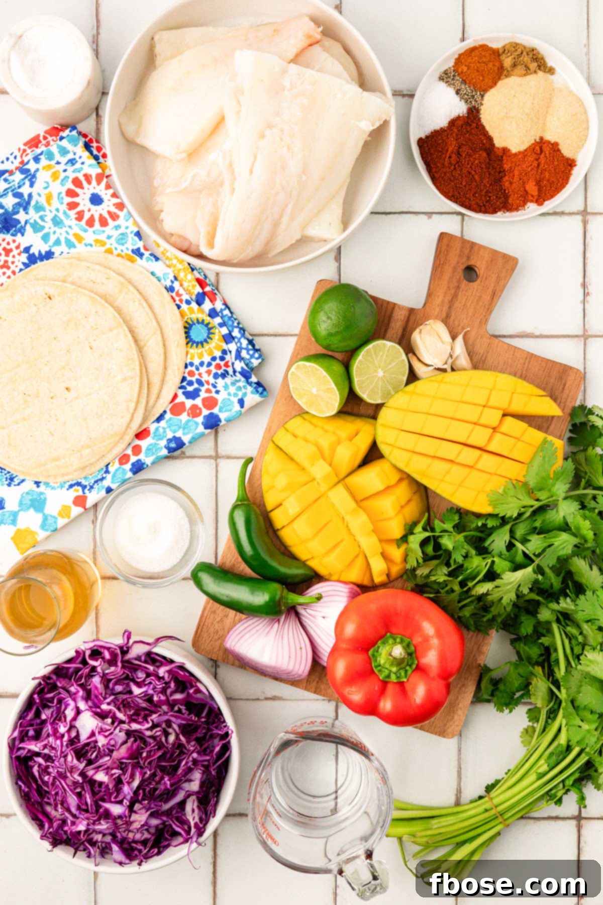 An overhead photo of various fresh ingredients laid out on a wooden table, ready to be prepared for fish tacos.