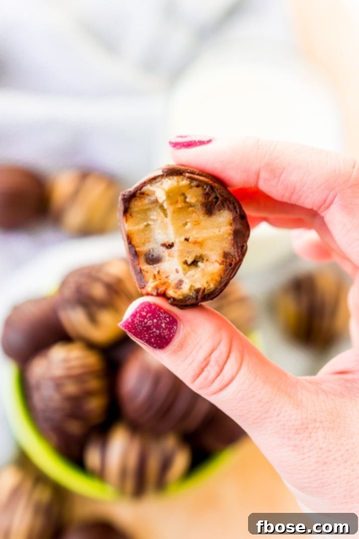 A woman's hand holding a cookie dough truffle that has been bitten into.