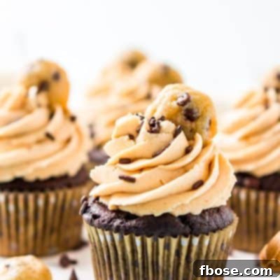 Chocolate cupcakes topped with peanut butter frosting and a mini cookie on a white cake stand.