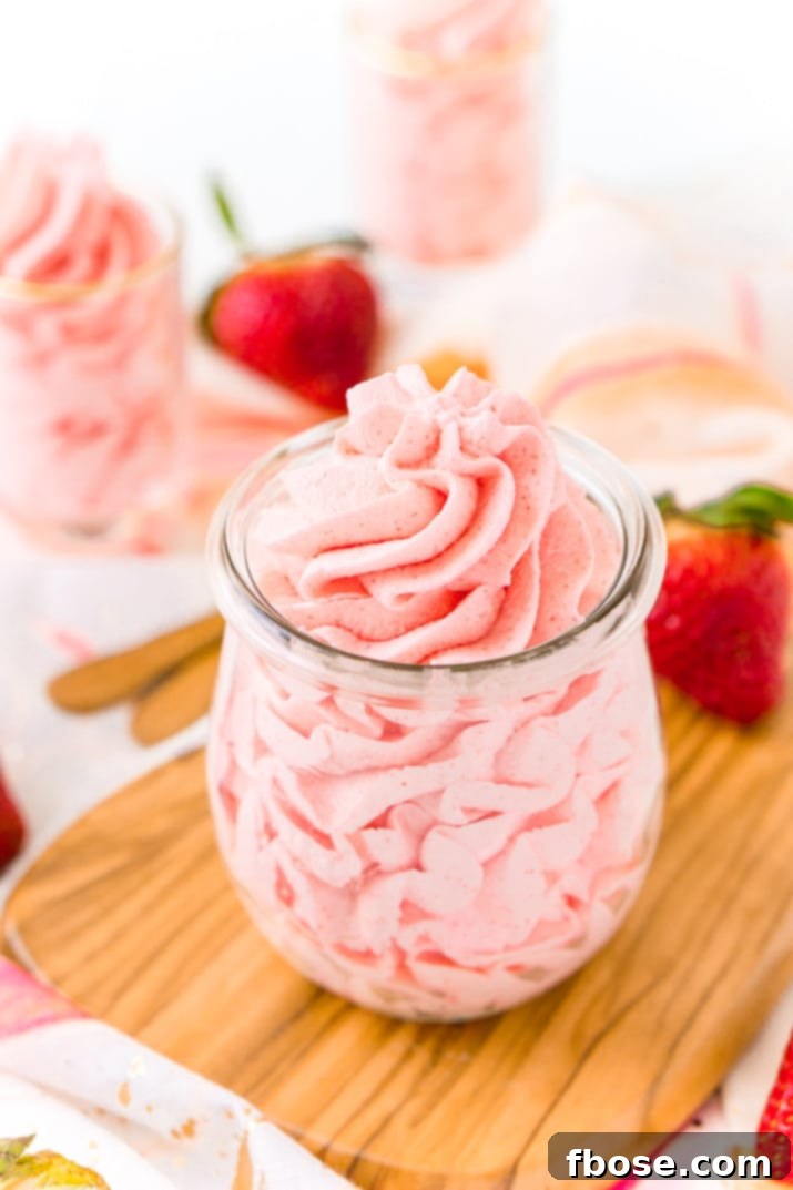 A bowl of creamy, pink strawberry frosting alongside the three simple ingredients: heavy cream, powdered sugar, and strawberry Jell-O mix, ready for mixing.