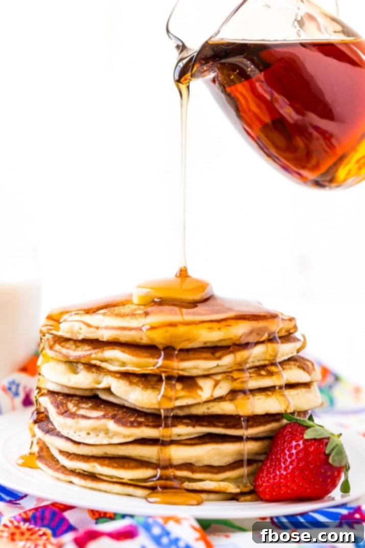 Pouring Maple Syrup generously over a tall stack of Homemade Buttermilk Pancakes