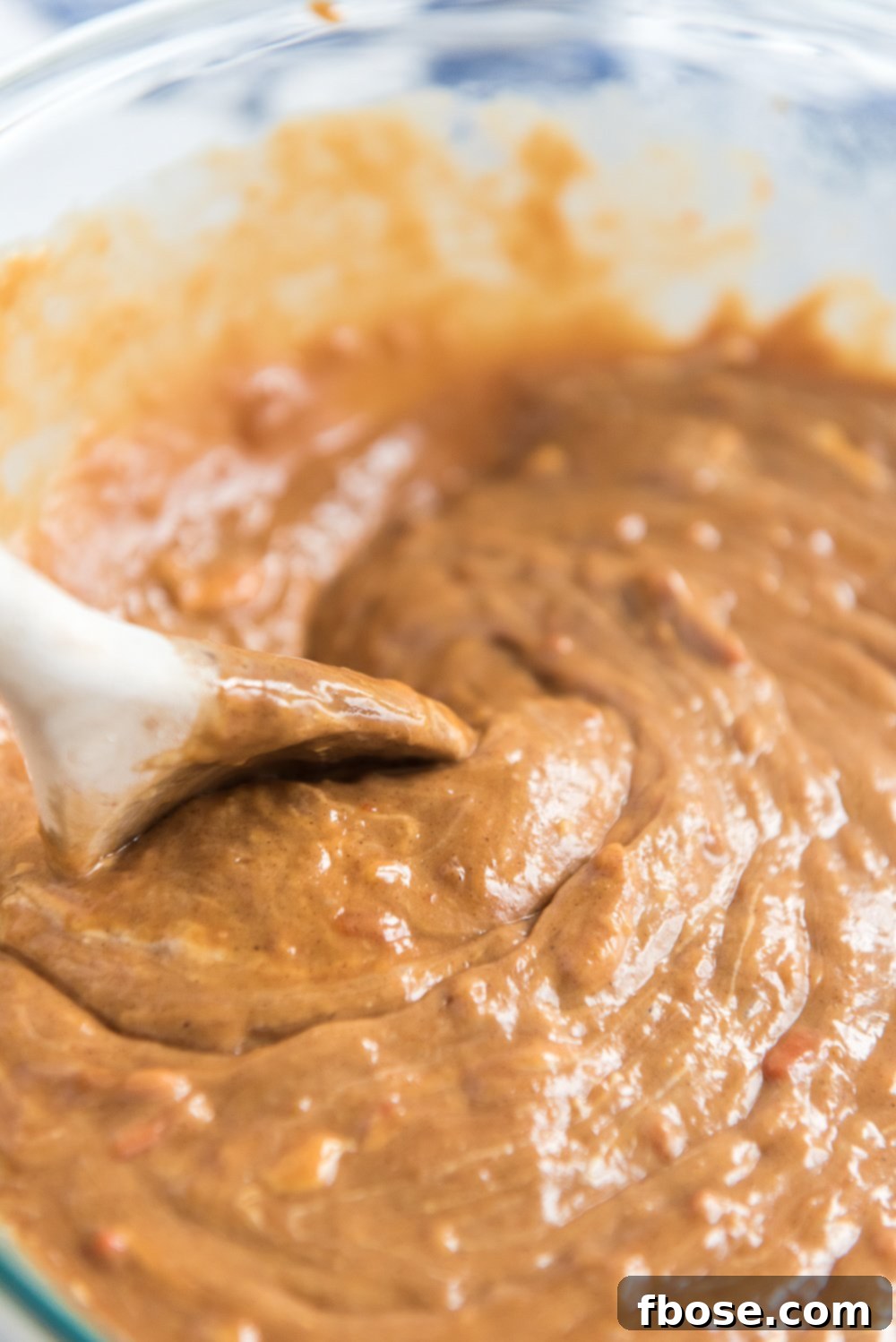 Batter for Caramel Carrot Cake in a bowl with a white mixing spoon.