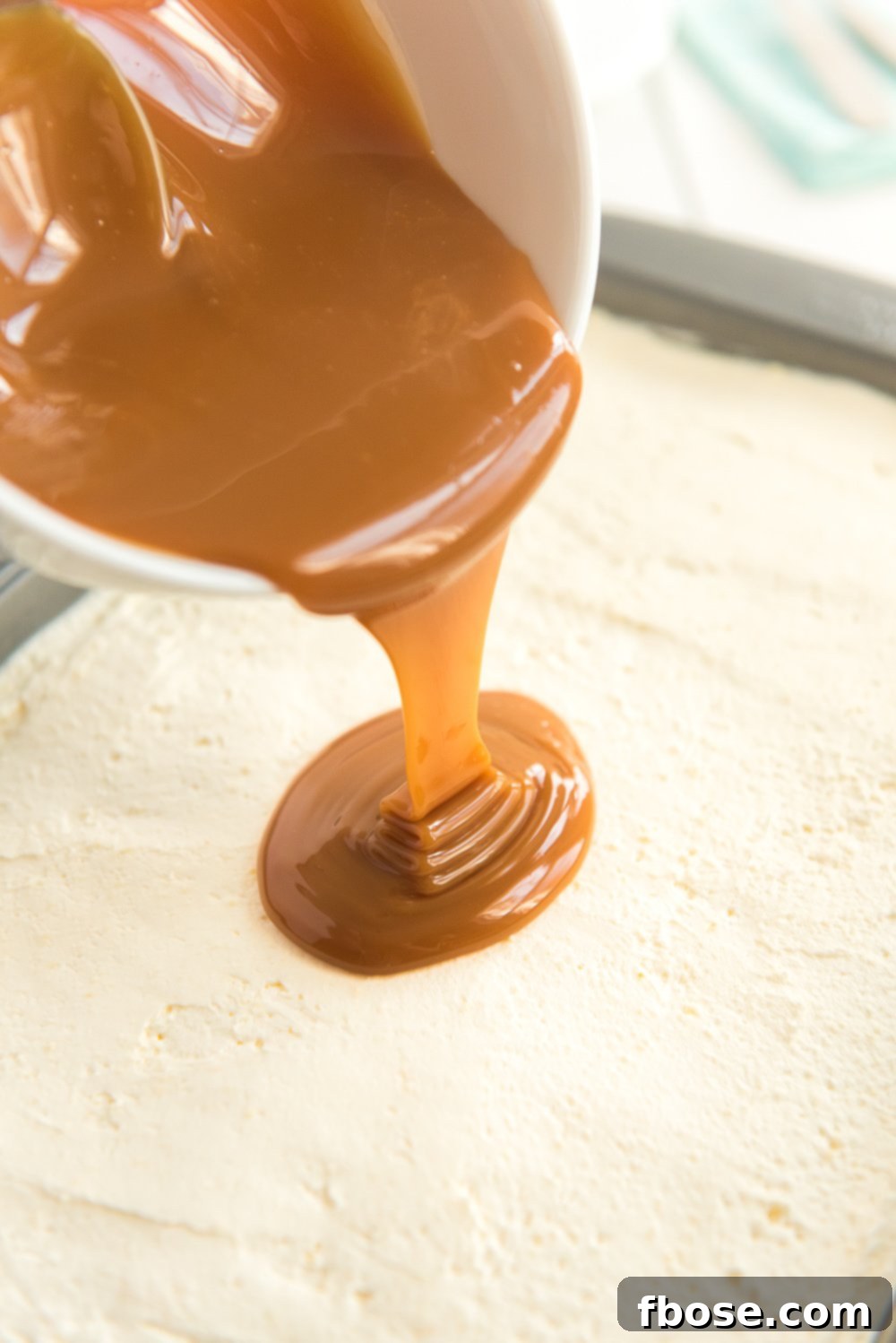 Caramel being poured over a frosted Carrot Cake.