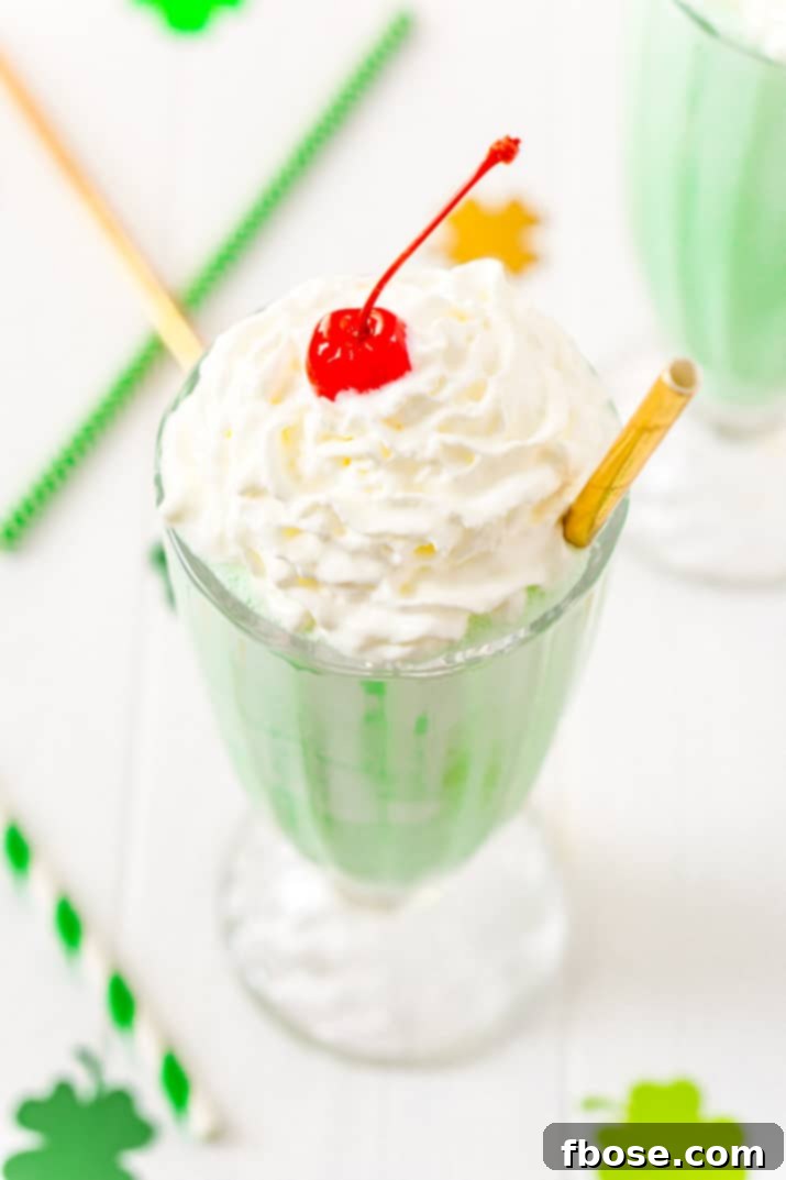 Shamrock Shake Recipe made with vanilla ice cream, milk, mint extract, food coloring, whipped cream, and maraschino cherries.