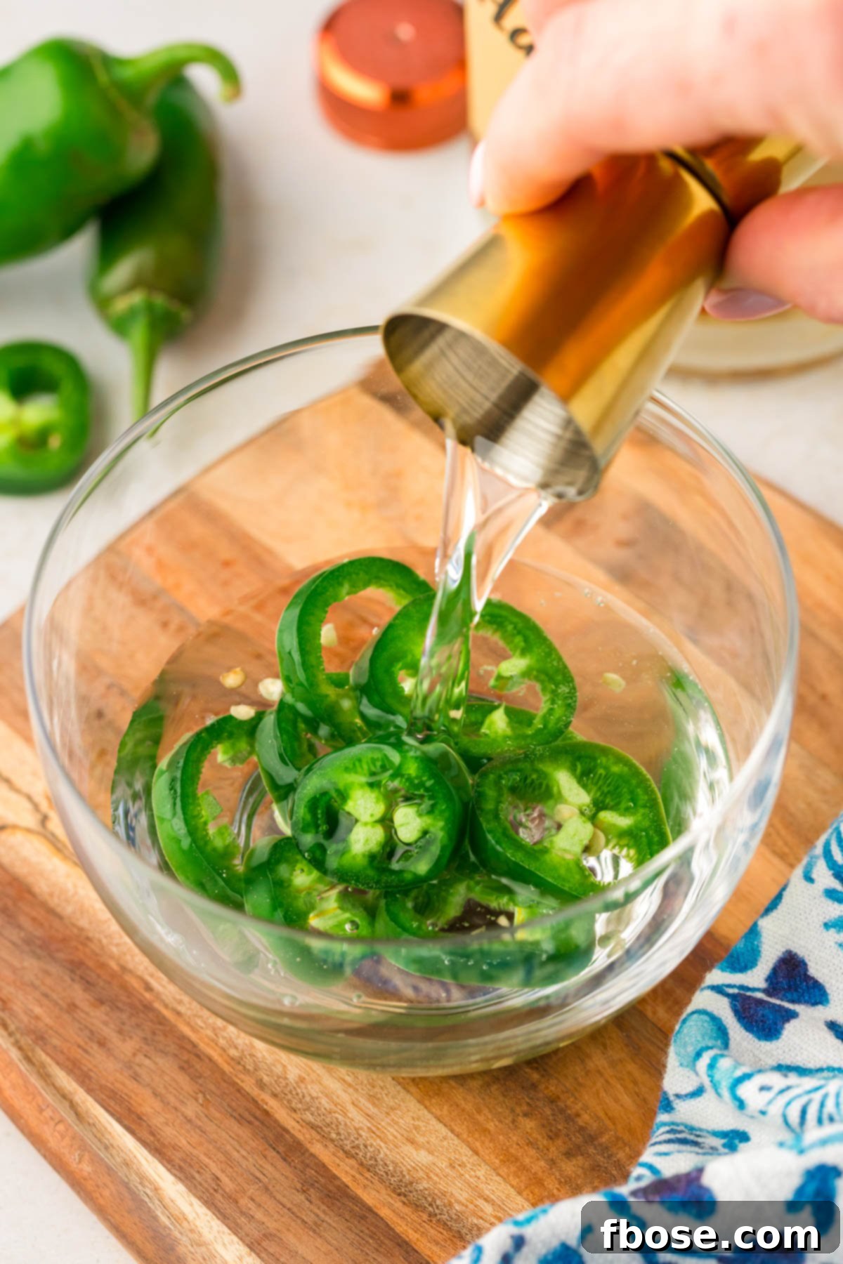 The Ultimate Bloody Mary Recipe 4 Vodka being poured into a small bowl with sliced jalapenos, illustrating the infusion process for a spicy Bloody Mary.